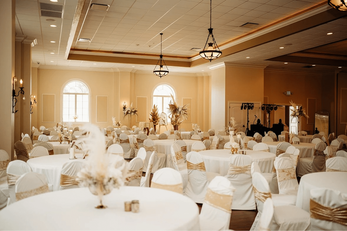 Elegant dining setup with round tables and white chairs adorned with gold ribbons.