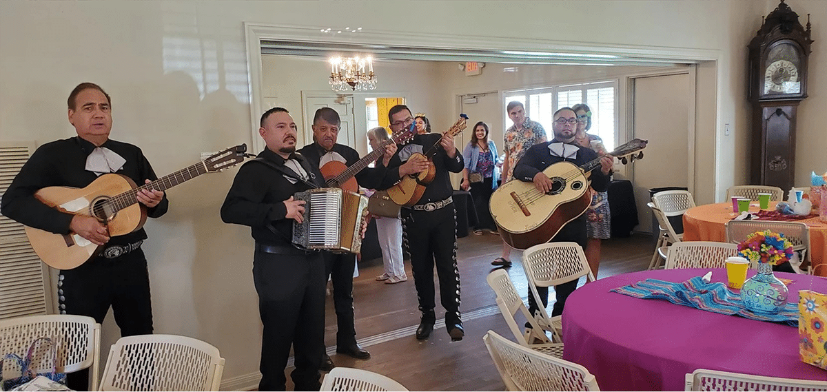 Mariachi band performing at a festive event with colorful tables in the background.