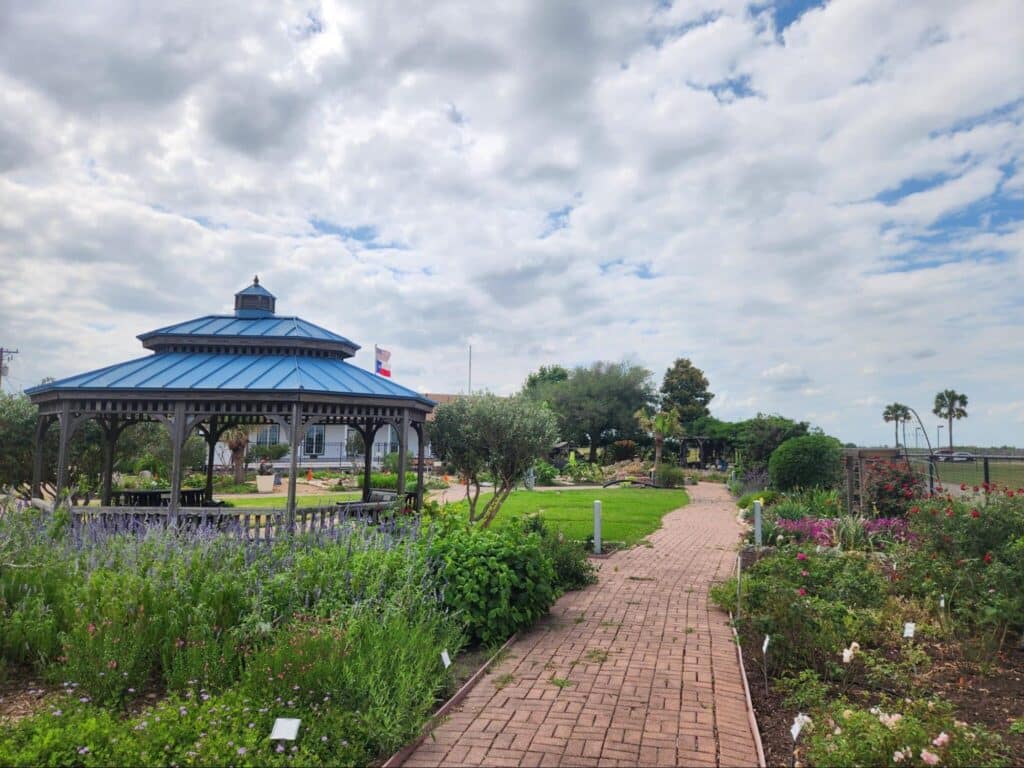 Garden path with gazebo under cloudy sky.